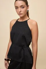Top negro de calce relajado y textura satinada, con escote halter y lazo fino para ajustar en la cintura.