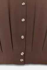 Camisa corta de cuello solapa y manga larga, con trabillas decorativas en los hombros. Presenta pliegues delanteros, elástico en la espalda y cierre frontal con botones.