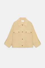 Chaqueta color beige con cuello solapa, manga larga remangada con trabilla y botón, y bolsillos de plastrón en el delantero. Cierre frontal con botones.