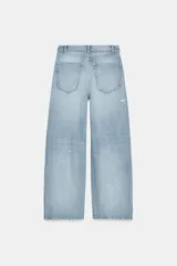 Jeans de mezclilla azul claro, tiro bajo, con corte ancho y pierna recta. Presenta un detalle de cintura cruzada o vuelta con un nudo o pliegue frontal y un ligero desgaste en una de las piernas.