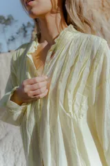 Camisa amarilla de algodón, corte suelto y largo asimétrico, más larga atrás que adelante. Tiene mangas largas amplias.