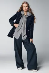 Pantalón cargo de tiro medio color azul oscuro, con pierna ancha y bolsillos de plastrón con solapa en las piernas. Presenta cierre frontal con cremallera, botón y ganchos metálicos.