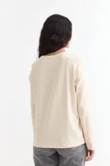 Remera de manga larga color beige con cuello redondo a la base. Presenta un estampado frontal con un dibujo de labios en color fucsia y la palabra 'BESITO' en color negro.