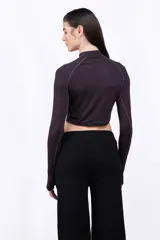 Remera cropped de manga larga con cuello alto, confeccionada en tejido elástico color negro. Presenta costuras visibles y un pequeño logo aplicado en el centro del pecho.