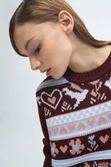 Buzo tejido de punto con diseño jacquard que presenta motivos de corazones, flores y aves en tonos bordó, blanco y celeste. Posee cuello redondo, puños y ruedo acanalados.