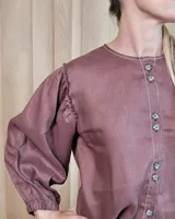 Camisa de manga larga con diseño de rayas verticales y bordados sutiles. Presenta cuello redondo, cierre frontal con botones y mangas abullonadas con volados en los hombros.