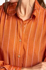 Camisa oversize color ladrillo con rayas verticales blancas y rosadas, de mangas largas y botones de madera.