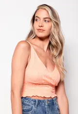 Top tejido color lila, sin mangas, con escote en V profundo y diseño cruzado en frente y espalda. Presenta calados y detalle de punto smock en la parte inferior.