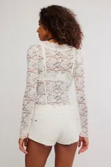 Remera de encaje floral blanca de manga larga y calce ajustado, con escote en V y diseño semitransparente.