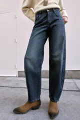 Jeans de tiro medio, color azul oscuro lavado, con corte balloon fit (holgado en muslos y estrechado en el tobillo). Presenta cinco bolsillos, cierre frontal con botones y detalle de trabilla con hebilla en la parte trasera de la cintura.