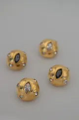 Par de aros dorados con forma circular, con un cristal negro central en forma de ojo de gato y pequeños cristales blancos alrededor.