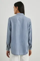Camisa celeste de denim tencel, de corte holgado, con cuello clásico, cierre frontal con botones y bolsillo en el pecho con detalle bordado.