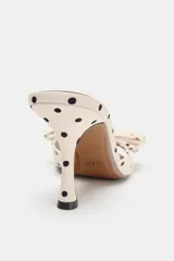 Sandalia tipo mule color crema con estampado de lunares negros, detalle de lazo en la parte delantera, tacón fino alto y punta fina.