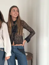 Pantalón de jean azul con cintura baja y corte de pierna ancha. Tiene cierre y botón en la parte delantera, bolsillos delanteros con detalle de encaje, bolsillo trasero plaquet y pasacintos.