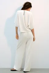 Top blanco de tejido rústico, con cuello redondo y mangas cortas amplias. Bajo recto.