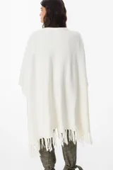 Ruana de tejido suave y envolvente en color blanco, con diseño de corte amplio y terminación de flecos en el ruedo.