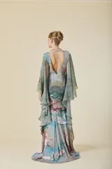 Vestido largo de corte sirena con escote en V, confeccionado en tela con estampado artístico de paisaje natural. Presenta mangas amplias y fluidas tipo capa en gasa semitransparente, que aportan movimiento y elegancia al diseño.