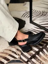 Zapato tipo slingback color negro, con plataforma y taco cuadrado. Presenta una puntera cuadrada y cierre con hebilla metálica en la tira trasera.
