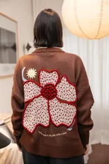 Saco tejido color chocolate con diseño inspirado en la granada, con flores y soles bordados. Presenta cierre frontal con botones, cuello redondo y puños acanalados.
