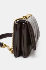 Bolso mini bandolera de efecto acolchado, color marrón oscuro, con pespuntes verticales. Posee asa de cadena dorada que puede usarse como doble asa de hombro. Cierre mediante solapa y botón imantado.