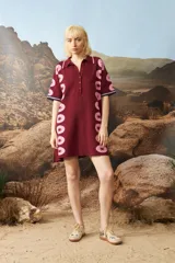 Vestido corto de tejido jacquard en color bordó con estampado de estrellas rosadas en los laterales. Presenta cuello polo con cierre frontal de botones y mangas cortas con terminación en contraste.
