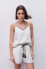 Blusa blanca de calce relajado y caída fluida, con escote en V, breteles finos y detalle de bordado en contraste en el escote y ruedo.