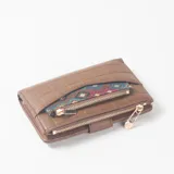 Billetera de cuero sintético marrón con diseño texturizado en bloques, cierre perimetral de cremallera con tirador metálico decorativo y un bolsillo frontal aplicado con detalle de tela estampada geométrica y cierre propio.