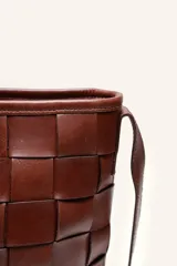 Cartera tipo morral de cuero color beige, con diseño trenzado artesanal, correa larga regulable y cierre superior.