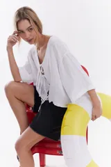 Blusa de lino color blanco, con mangas cortas amplias, escote en V y cierre frontal mediante lazos con moños.