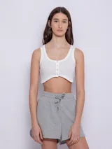 Top blanco de tela texturada, sin mangas y con cuello redondo. Cuenta con cuatro botones y terminación en curva en la parte delantera.