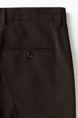 Pantalón sastrero de corte slim fit en color marrón, con pliegues frontales, cierre de botón y trabillas para cinturón.