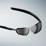 Lentes de sol envolventes con montura de acero inoxidable en acabado plateado cepillado y lentes de nylon espejadas. Presentan un diseño vanguardista con aberturas decorativas en la parte superior del marco.
