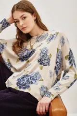 Sweater de punto con diseño estampado de flores en tonos azules y verdes sobre base color crema. Presenta cuello redondo y mangas largas con corte holgado.