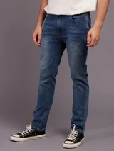 Jean de corte slim fit con cintura media, confeccionado en denim azul con efecto de lavado desgastado.