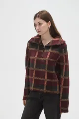 Sweater de tejido jacquard con diseño a cuadros en tonos bordó, negro y beige. Presenta un corte holgado, cuello solapa amplio y cierre frontal parcial con cremallera.