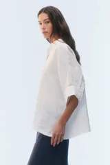 Camisa oversize blanca de lino, con corte cuadrado, mangas raglán cortas con puños anchos, aberturas laterales y cierre frontal de botones.