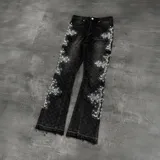 Pantalón de jean negro de corte flare, con diseño de cruces formadas por apliques de strass a lo largo de las piernas.