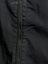 Campera negra con capucha y cierre frontal con cremallera. Tiene puños elásticos y un pequeño parche con el logo de la marca en el pecho.