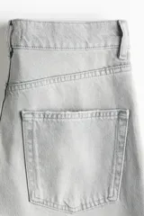 Jean barrel de tiro alto confeccionado en denim de algodón rígido color gris claro con efecto deslavado, diseño curvo en las piernas y tiras finas para anudar en los bajos.