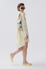 Camisa amarilla a rayas verticales blancas, de calce holgado y hombros caídos, con botones al frente.