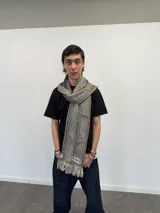Bufanda larga de tejido trenzado con diseño de cuadros en tonos beige, marrón, negro y blanco. Presenta flecos en los extremos, una grifa de goma con logo en una punta y una etiqueta tejida con logo en la otra.