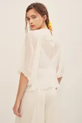 Camisa blanca de manga larga abullonada, con cuerpo de red transparente con bordados florales en tono crudo y aplique de flor grande fucsia en el hombro.
