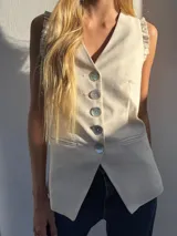 Chaleco largo color crudo confeccionado en lino, con escote en V, botones de nácar y volados en los hombros. Diseño entallado.