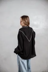 Camisa de color terracota con diseño de estilo western, presenta bordados blancos en la parte superior delantera y mangas largas abullonadas con puños ajustados. Cuenta con cierre frontal de botones y cuello camisero.