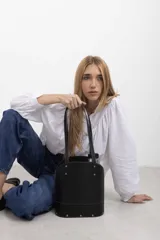 Cartera matera de cuero vacuno negro con textura símil lagarto, diseño estructurado con base ovalada y doble asa de hombro. Cuenta con detalles de tachas metálicas doradas y costuras pespunteadas en contraste.