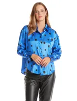 Camisa de satén de corte holgado con cuello camisero y cierre frontal de botones metálicos. Presenta un estampado de cuadrados negros sobre fondo azul vibrante, mangas largas con puños abotonados y un acabado brillante característico del satén.
