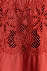 Blusa de viscosa color rojo óxido con secciones de broderie en el pecho y las mangas, cuello elevado festoneado y mangas globo al codo con puños elásticos.