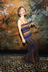 Vestido largo de punto con diseño a rayas horizontales en tonos azul, marrón y mostaza, con toques de brillo. Presenta corte ajustado en la parte superior con tirantes y falda larga con vuelo y movimiento.
