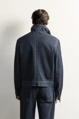 Campera de denim azul oscuro de corte cropped, con cuello camisero, bolsillos delanteros con solapa y cierre frontal oculto con botones metálicos.