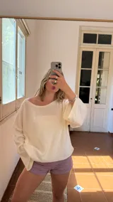 Blusa de tejido de punto color crudo con hilos de lurex que le dan un brillo sutil. Presenta un escote bote que puede usarse recto o caído sobre un hombro.